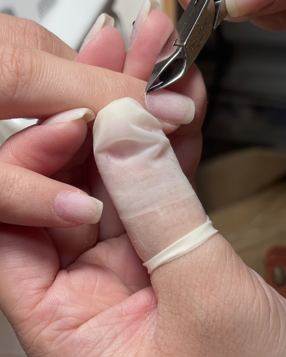 A close-up of stainless steel cuticle nippers being used to trim loose skin around the nail cuticle.