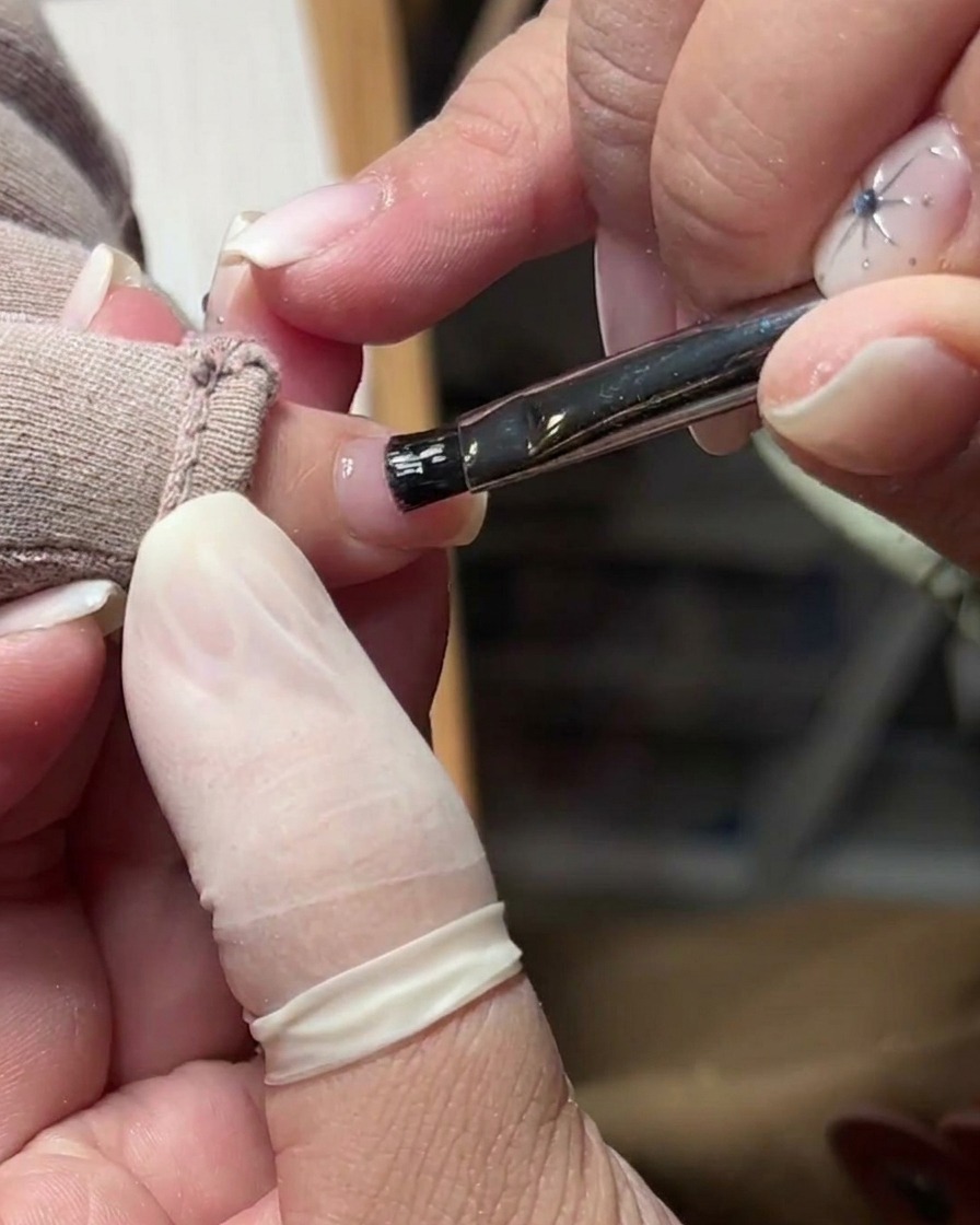 A soft brush removing dust and debris from the surface of a prepped natural nail.
