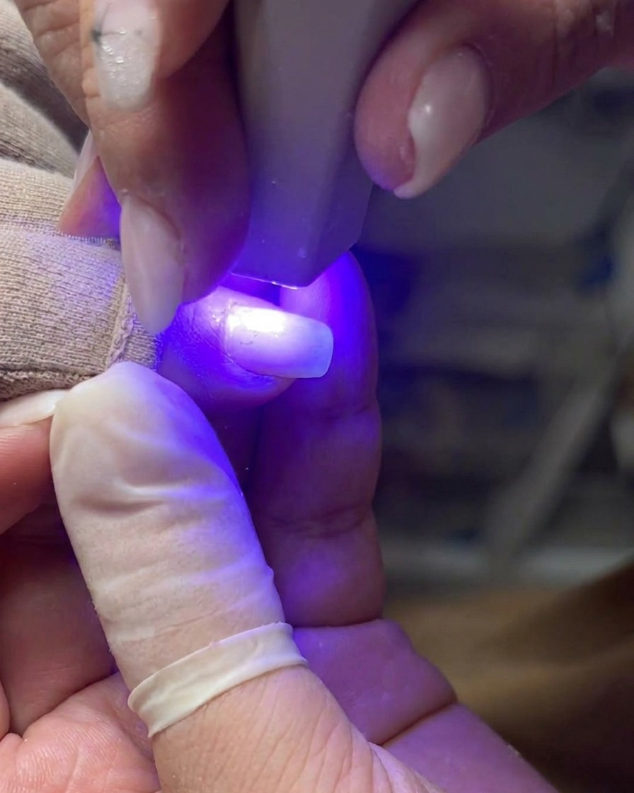 A professional nail brush applying an even layer of clear gel to a natural nail plate.