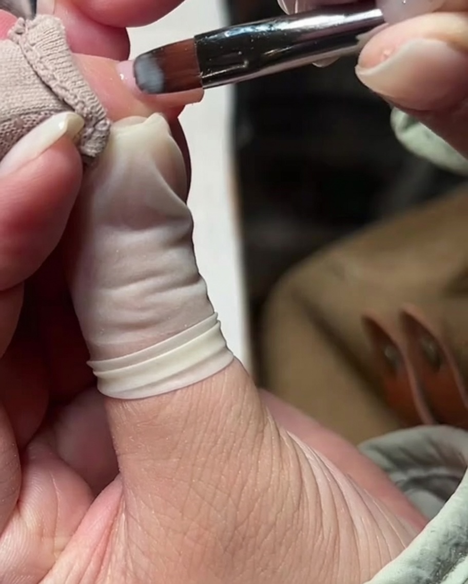 A gel brush applying a smooth, thin layer of milky nude gel polish over the nail surface.