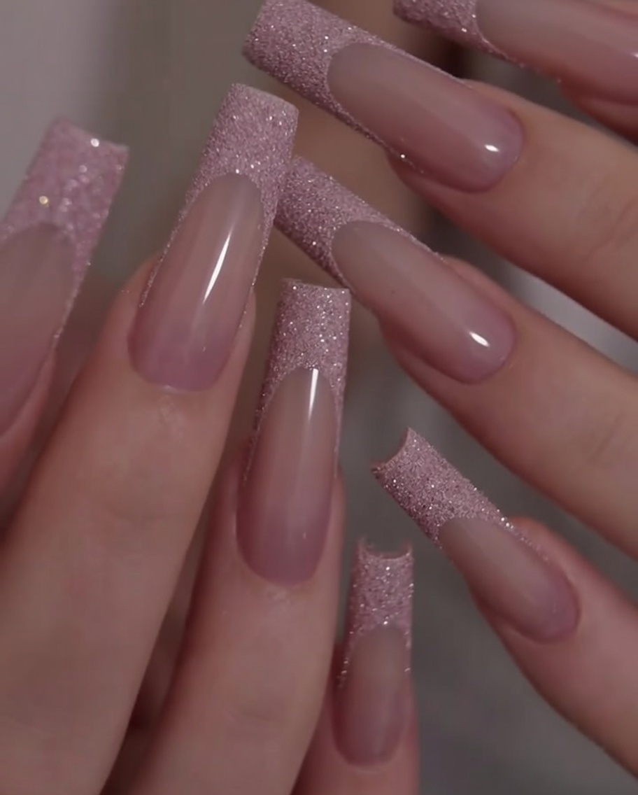 A close-up shot of hands being rotated to showcase the contrast between the pink base and the glitter French tips.