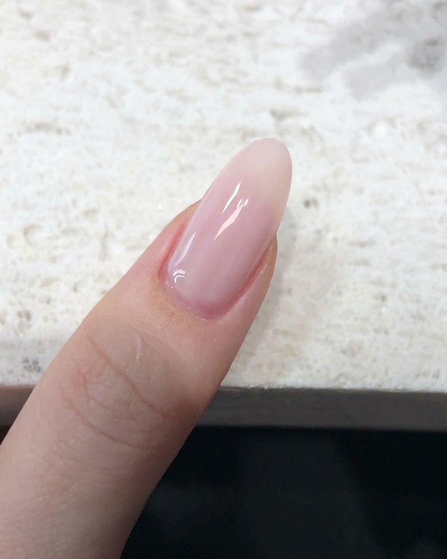 A close-up view of a fingernail coated in a sheer, nude-pink jelly polish with a smooth finish.