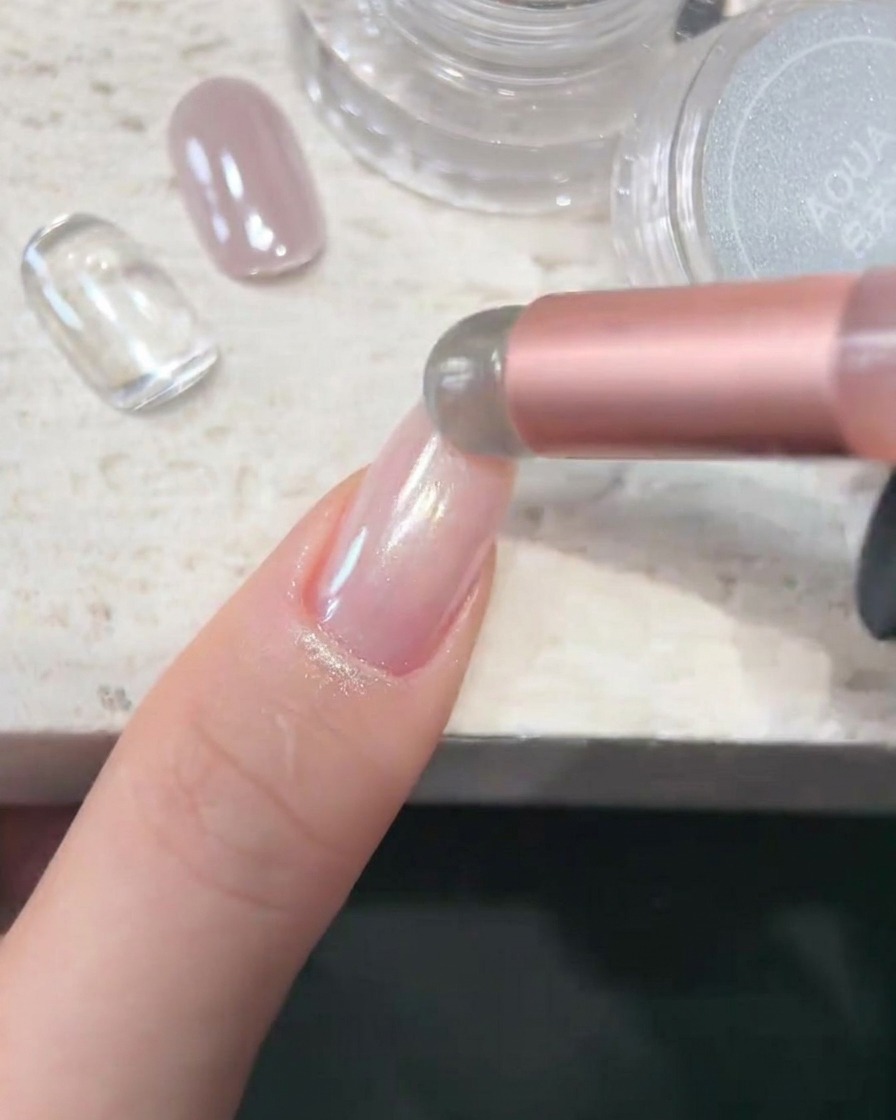 A sponge applicator depositing AQUA white chrome powder onto a smooth, glossy nail surface.