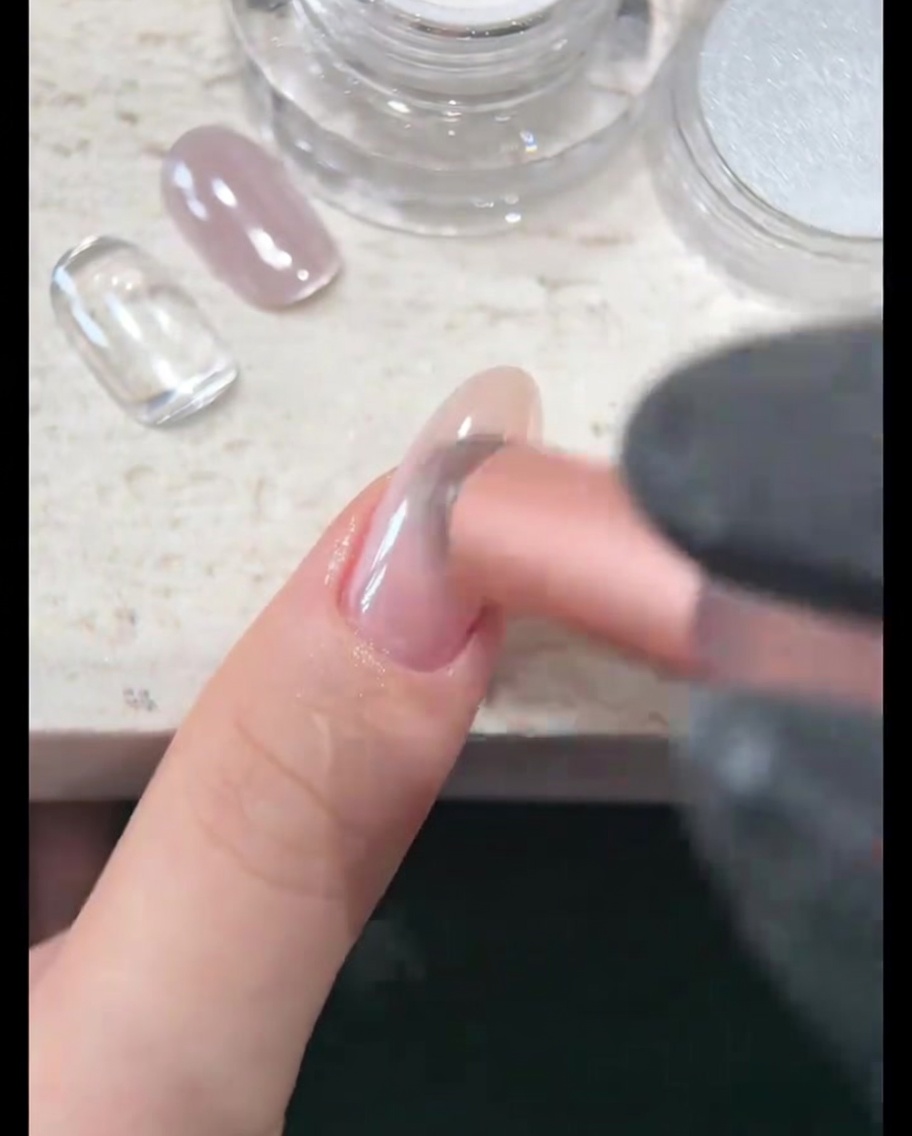 A close-up view of the nail surface being buffed until it shows a brilliant, pearlescent mirror shine.