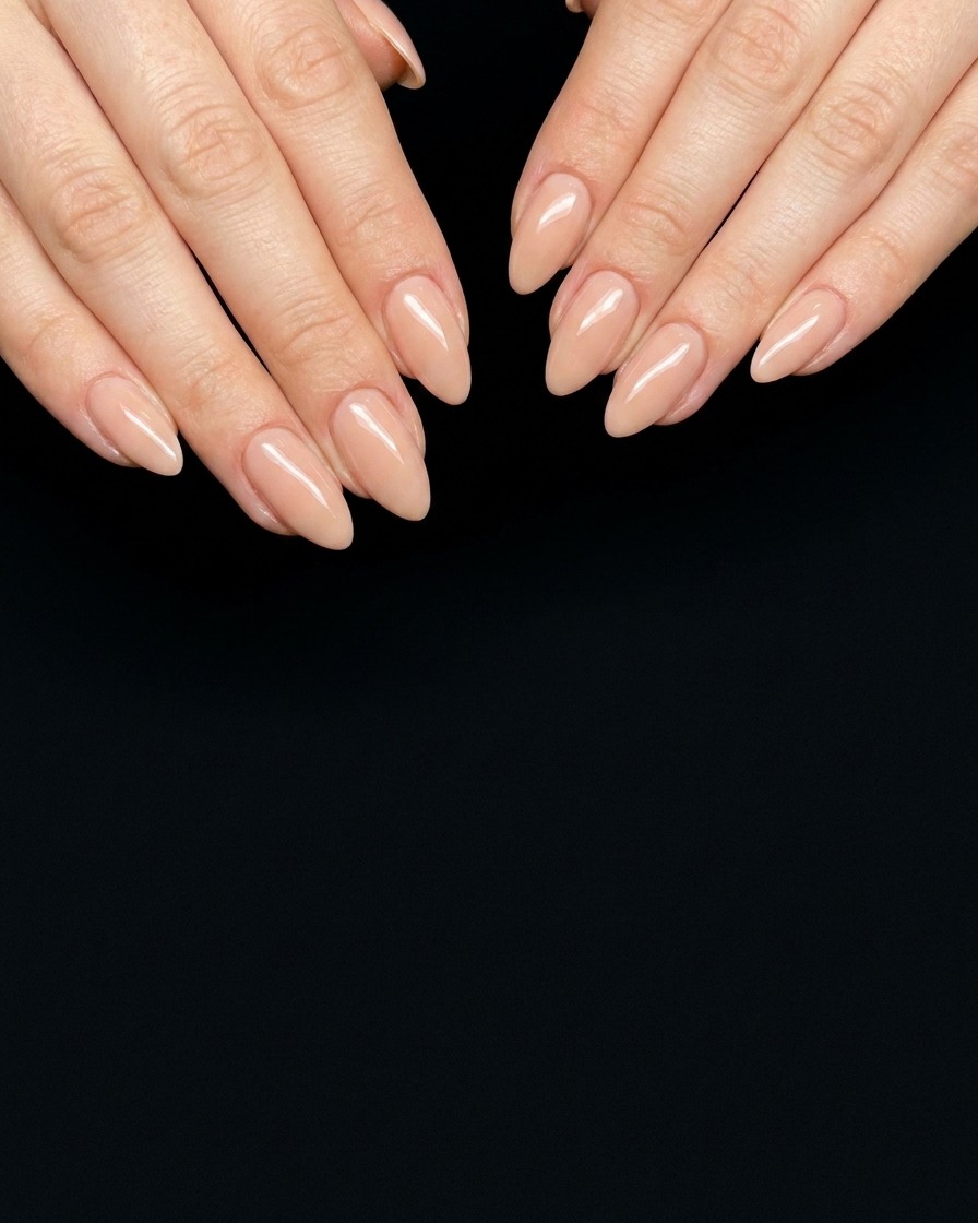 A close-up of a brush applying a sheer pink gel polish to a prepared, bare nail plate.