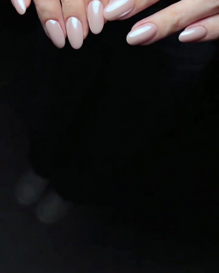 A close-up of a sponge applicator applying white iridescent pearl powder over a pink gel-coated nail.