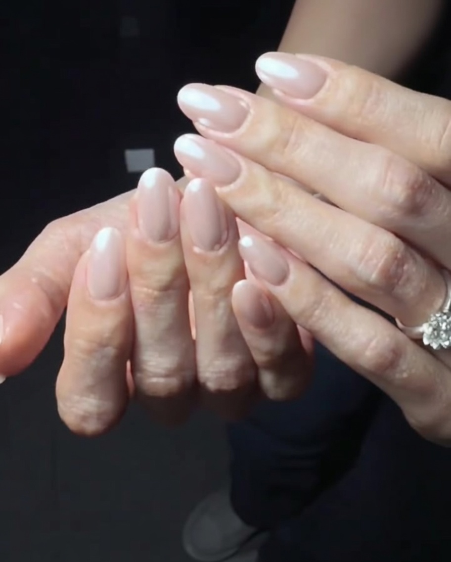 A close-up view of hands buffing the surface of nails coated with pearl chrome powder to refine the finish.