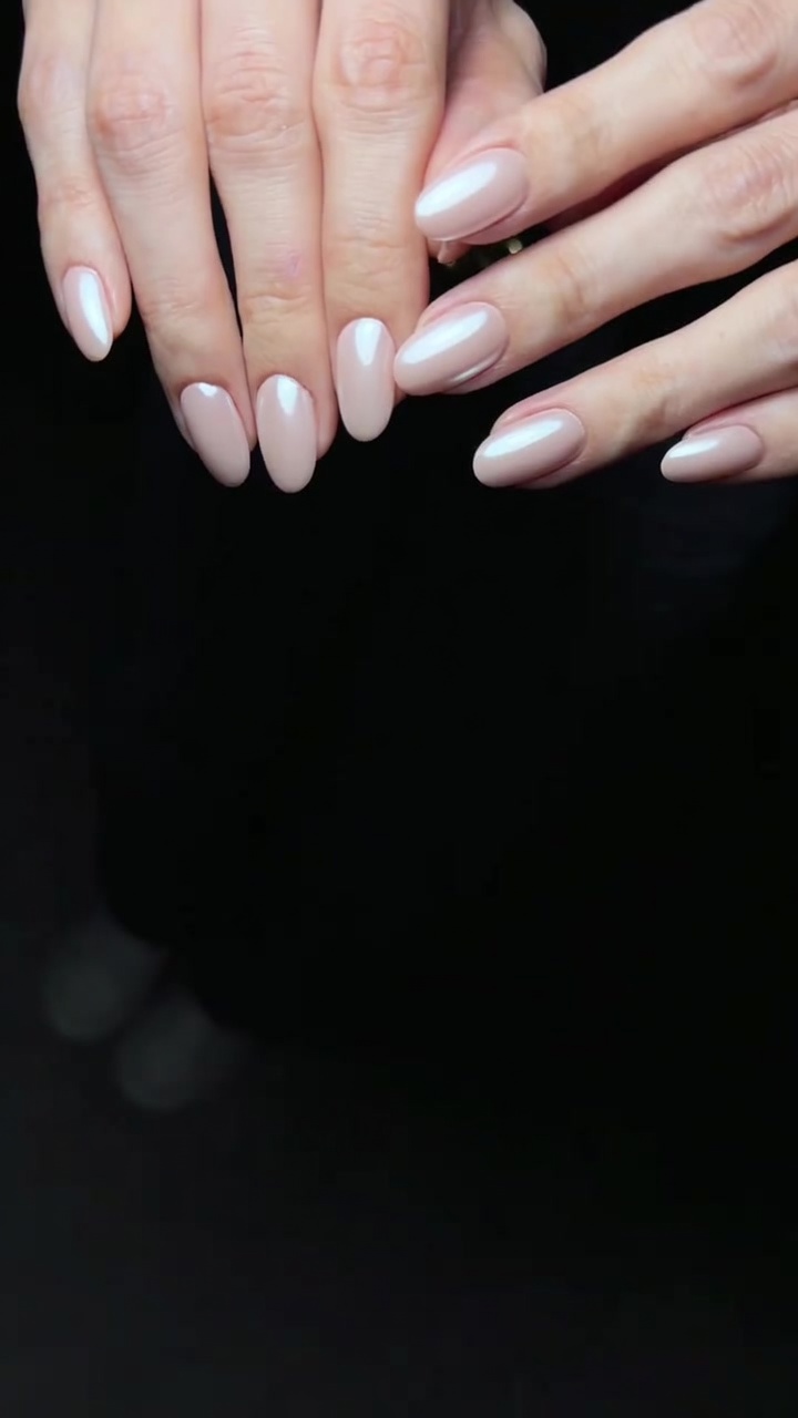 Close-up of elegant almond-shaped nails featuring a sheer pink gel base and a luminous pearl chrome finish.