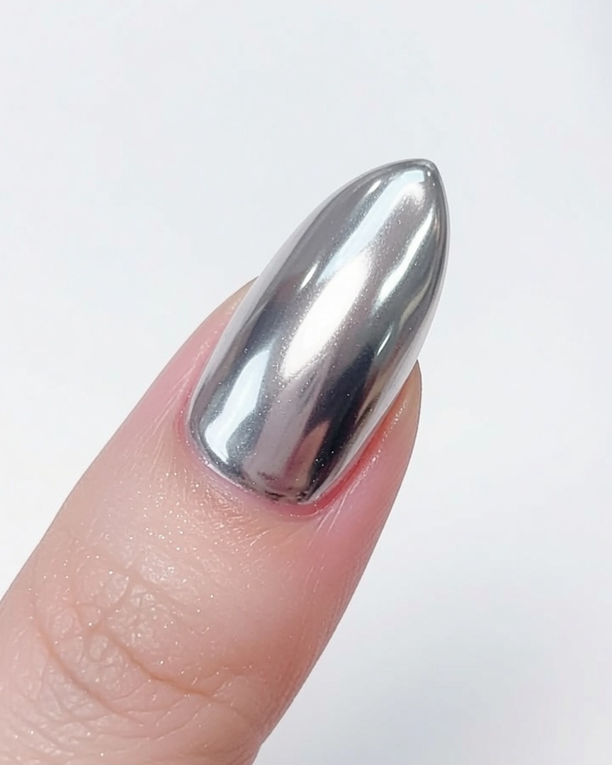 A fluffy brush being used to remove excess silver chrome powder from a finished mirror-effect nail tip.