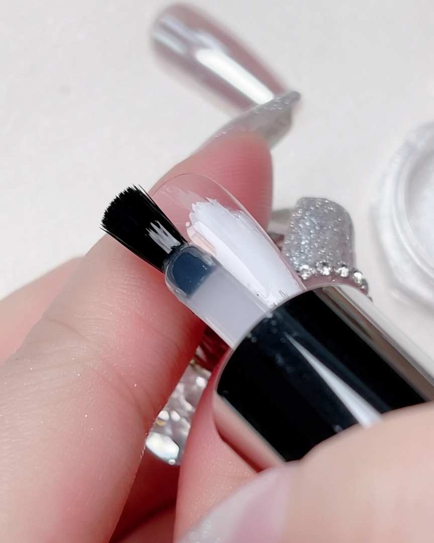 A thin clear top coat being applied with a brush specifically over the white center stripe of the nail.
