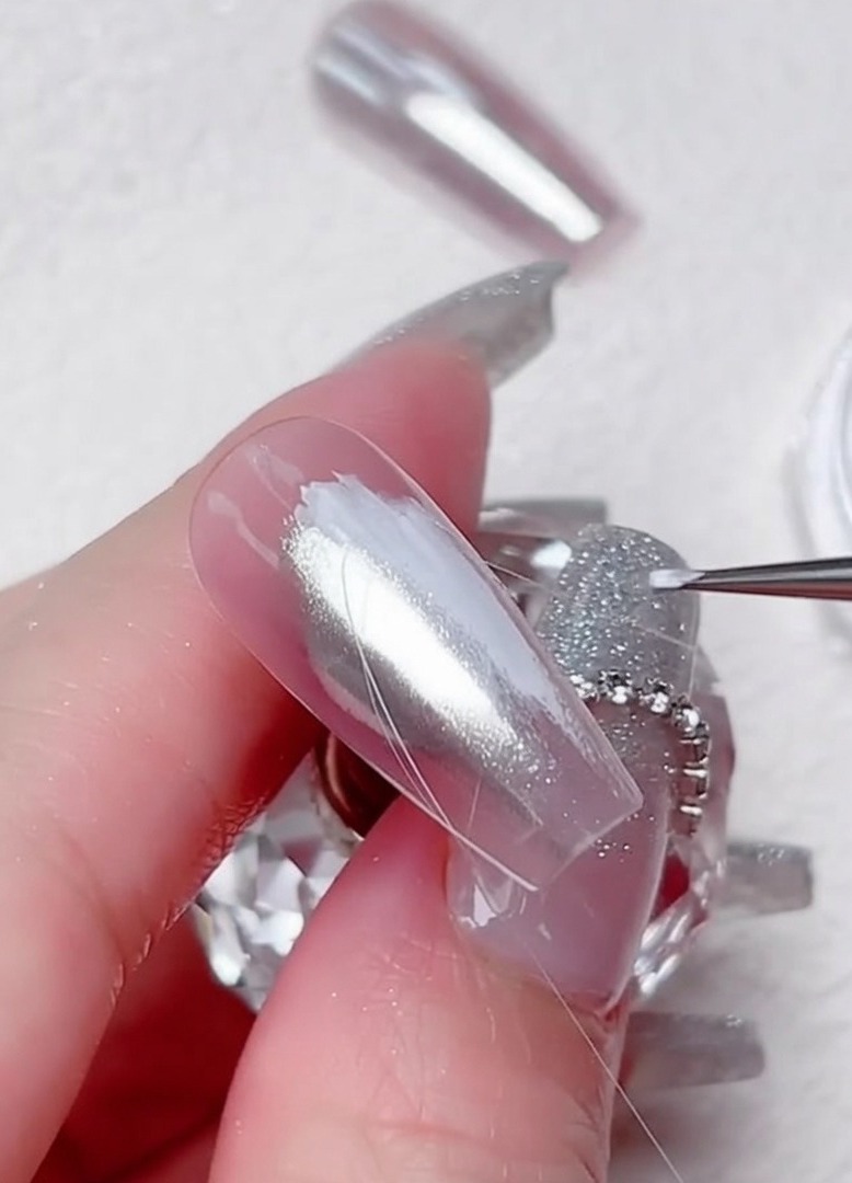 A fine liner brush drawing thin, clear gel lines in a diagonal pattern across a silver chrome nail.