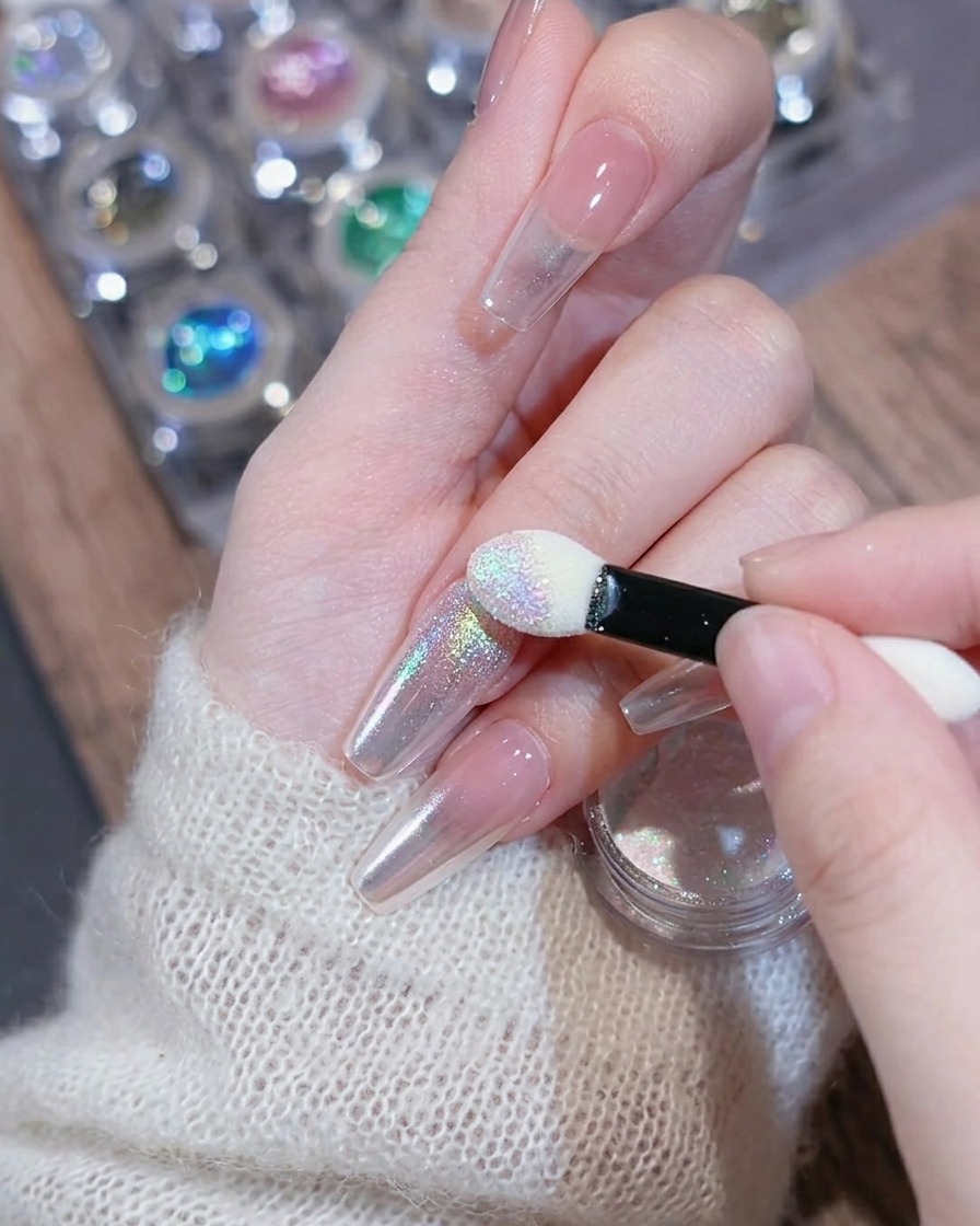 A sponge applicator applying shimmery pearl powder onto the nail tip.