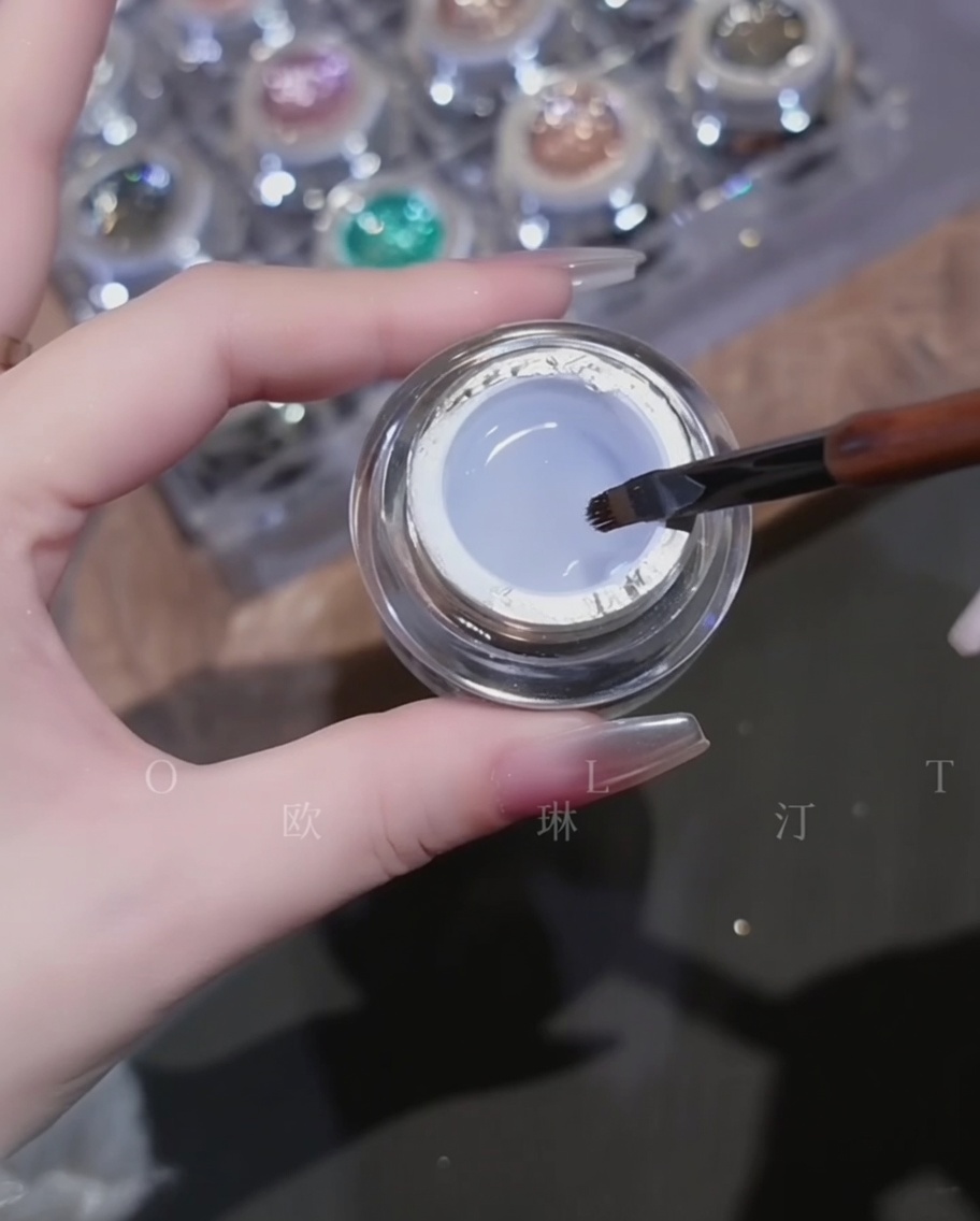 A brush applying a clear, viscous builder base gel over a chrome-finished nail.