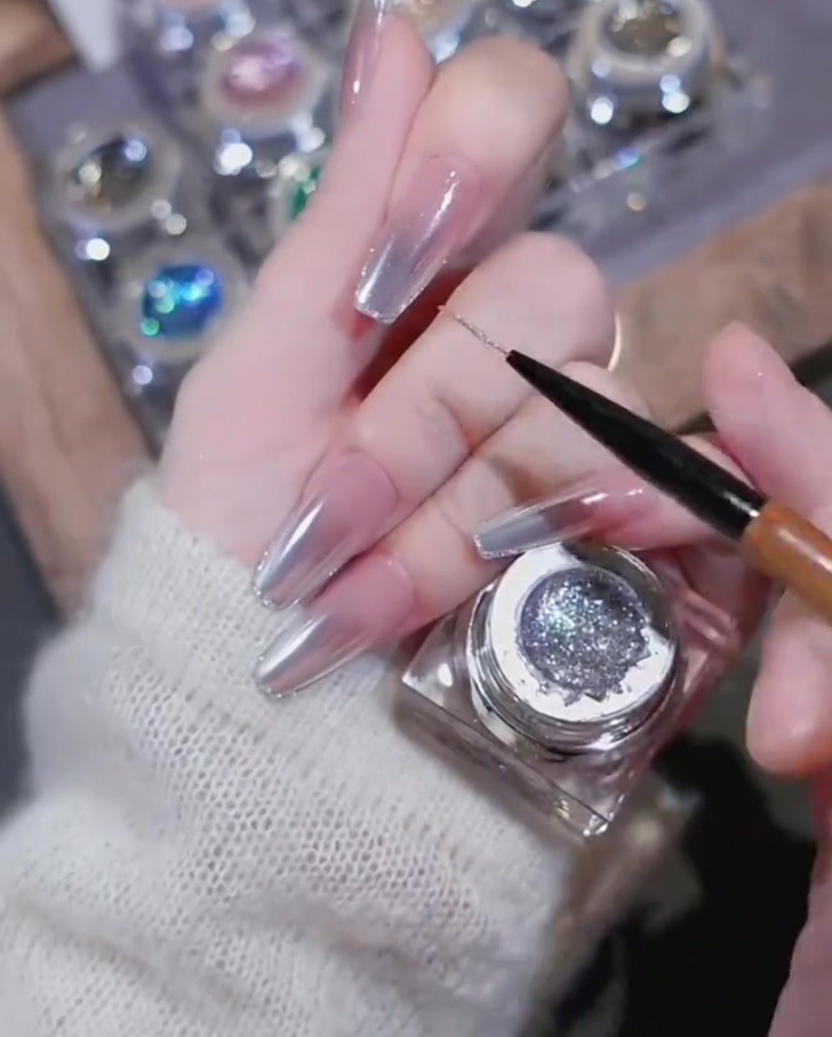 A close-up showing a heart-shaped rhinestone charm being placed onto a nail decorated with high-gloss gel lines.