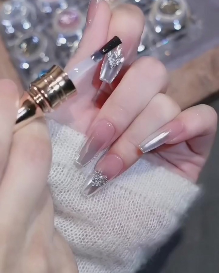 A top coat brush carefully applying gel around a heart-shaped diamond charm on a finished chrome nail.