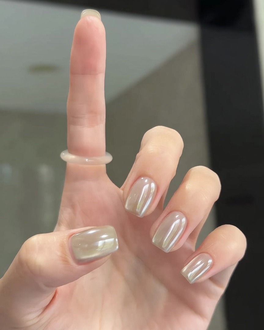 A soft brush buffing pearl chrome powder onto the surface of the nails for a smooth finish.