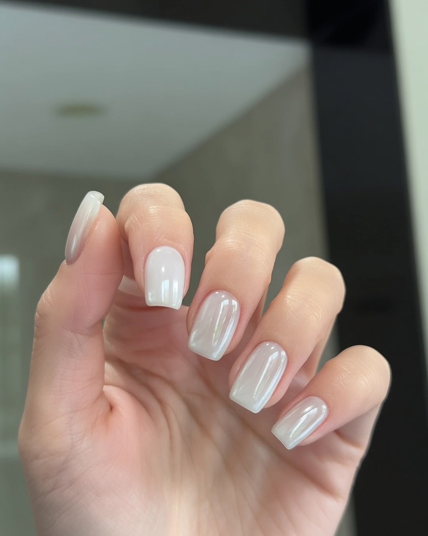 A brush applying a clear top coat layer over nails with a pearl chrome finish.