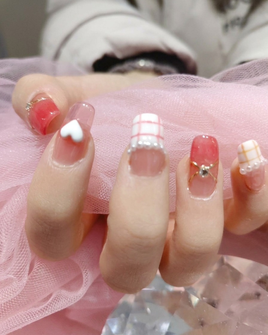 A tool placing tiny, iridescent white pearls around the base of the nail art designs on a manicured hand.