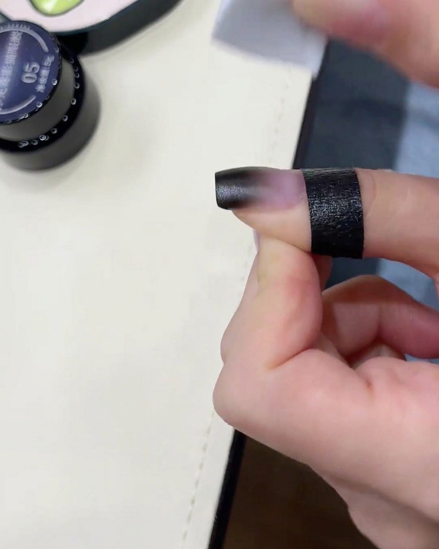 A sponge blending black gel on a nail.
