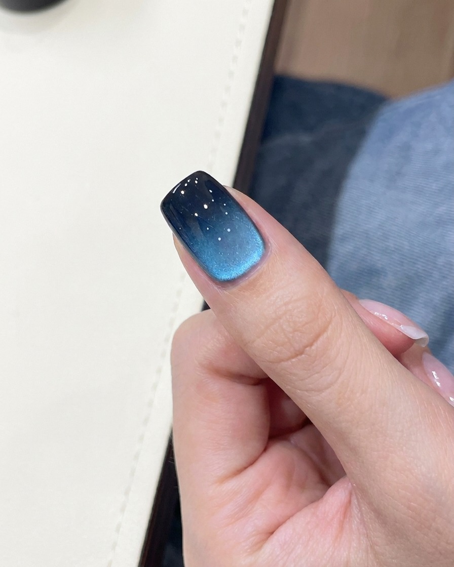 A close-up of a blue and black gradient nail with a small, gold-colored hollow butterfly sticker placed in the center.