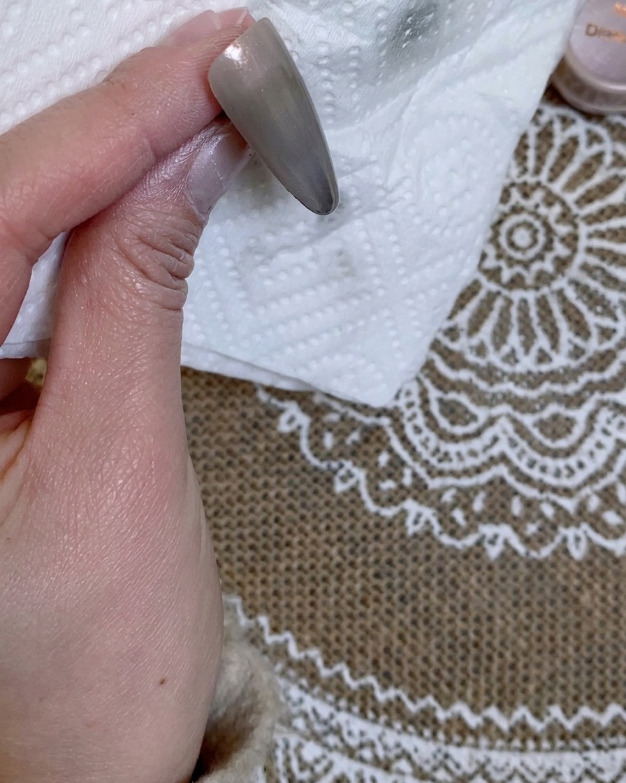 A close-up view of a grey-colored nail tip held against a white paper towel.