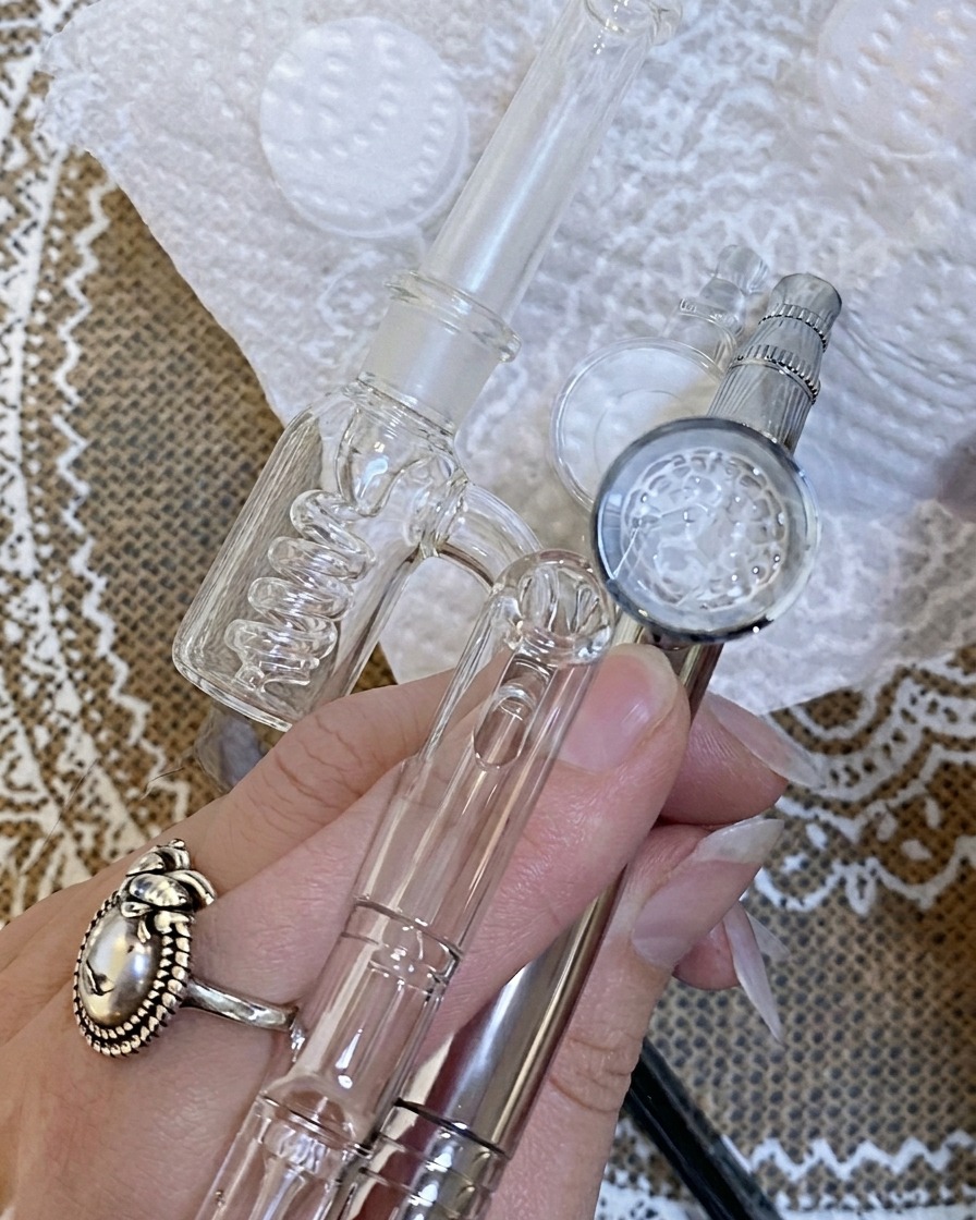 An airbrush being used to apply a fine mist of color onto a nail tip positioned over a white surface.