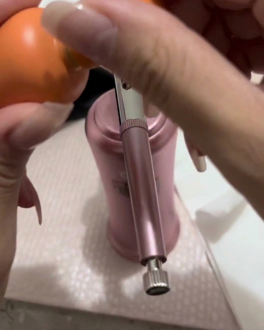 A small amount of peach-pink gel being transferred from a brush into the metallic cup of an airbrush gun.