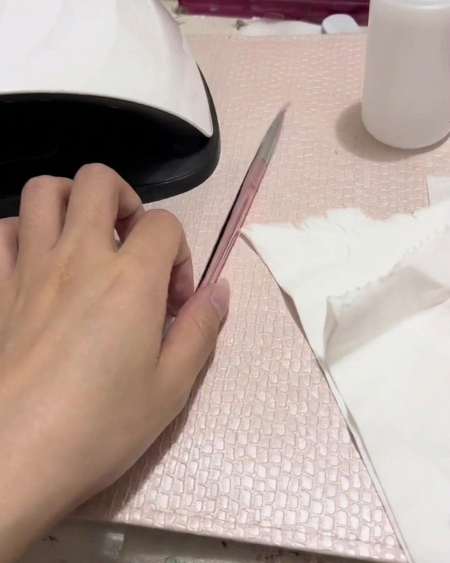 An airbrush being tested on a folded white tissue, showing a soft pink spray pattern.