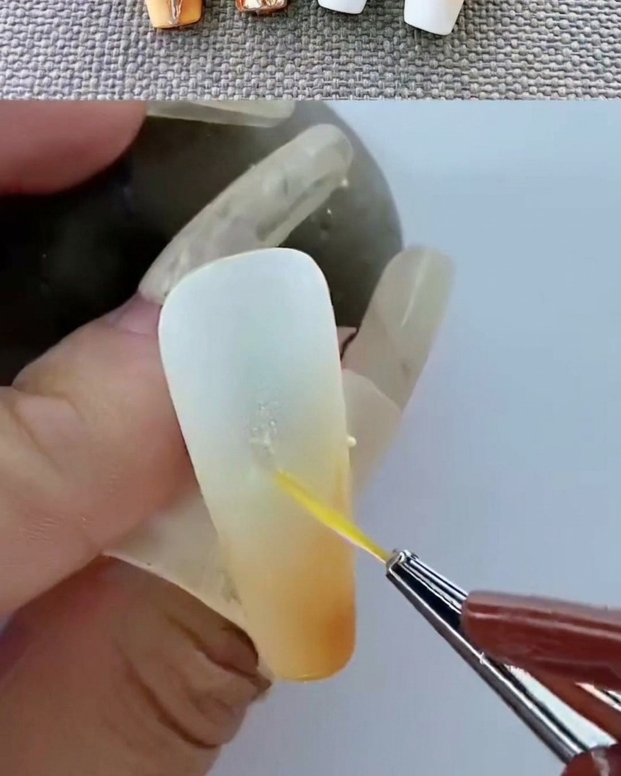 Tweezers placing a gold metal emblem onto an uncured gel surface.