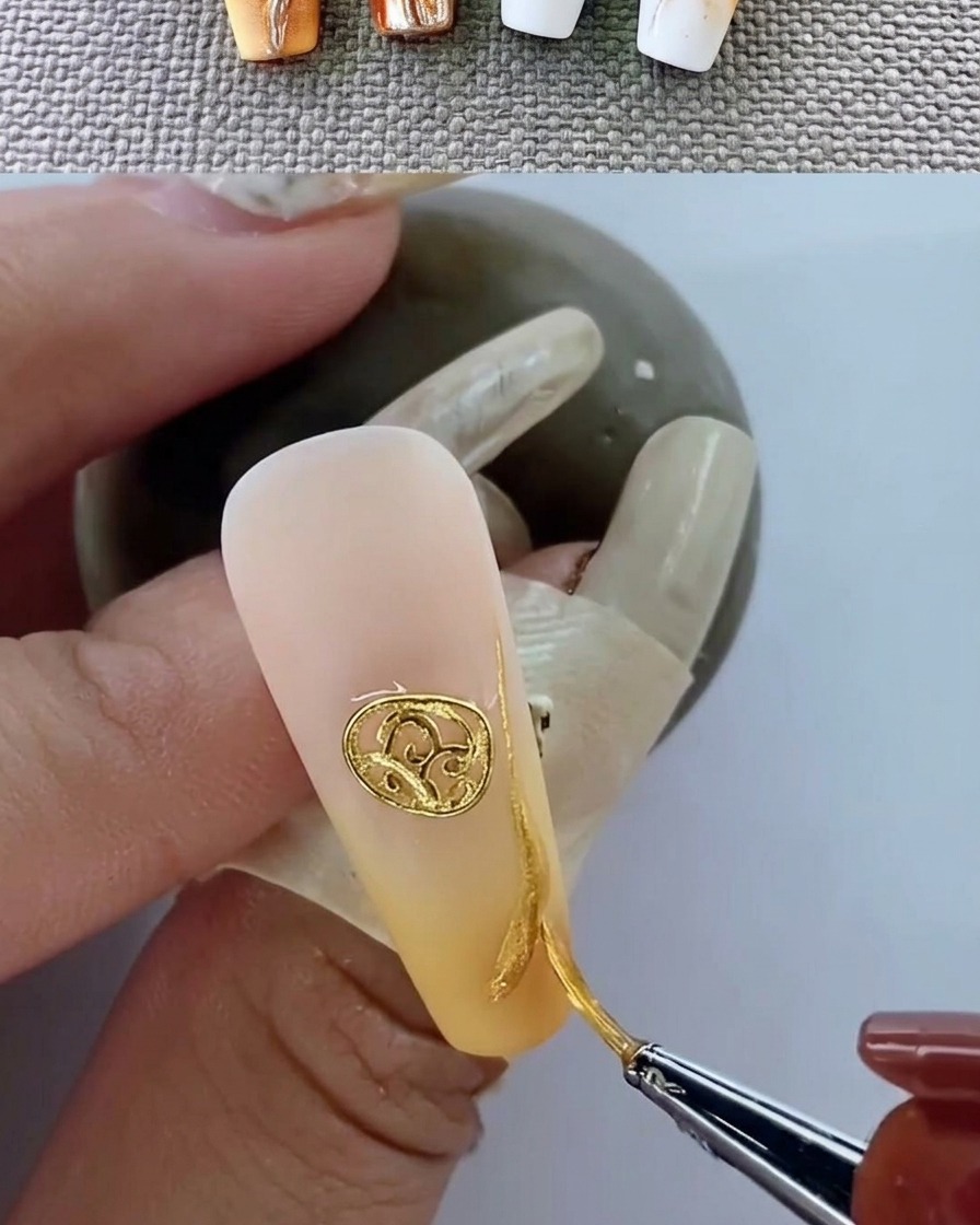 A close-up of a manicured nail with a metallic emblem curing under a UV lamp.