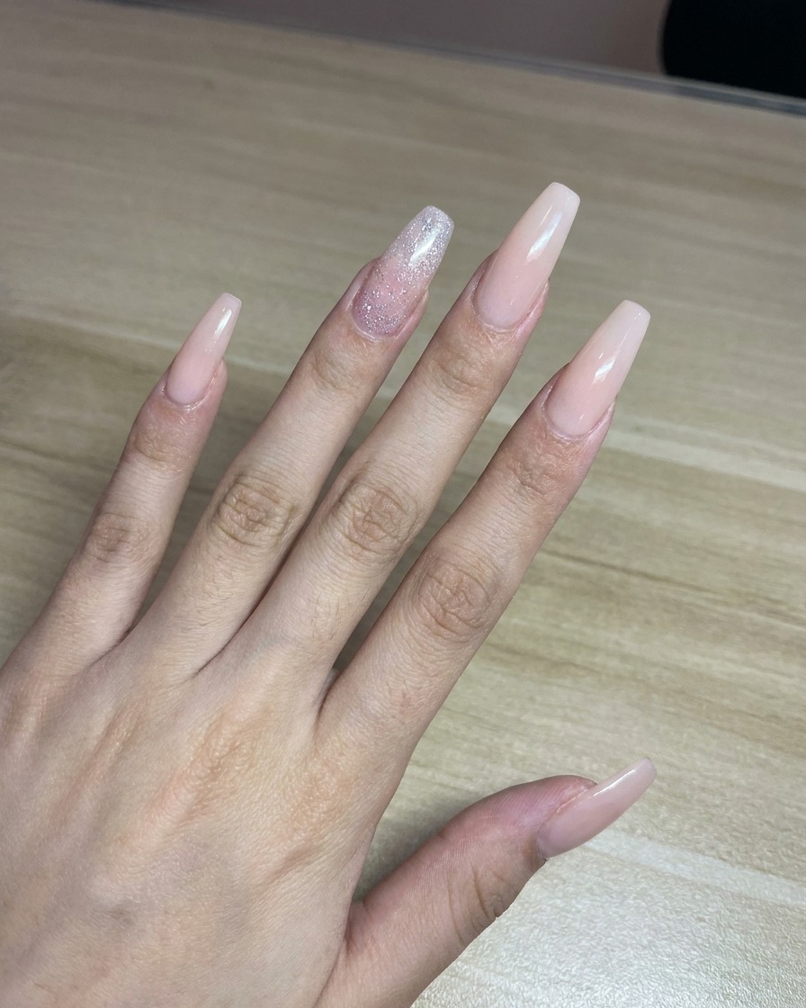 A technician spraying pink paint from an airbrush onto a piece of white paper as a test before applying it to nails.