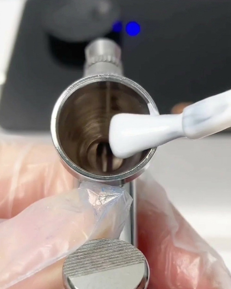 A brush adding a dollop of white gel polish into the metal airbrush cup.