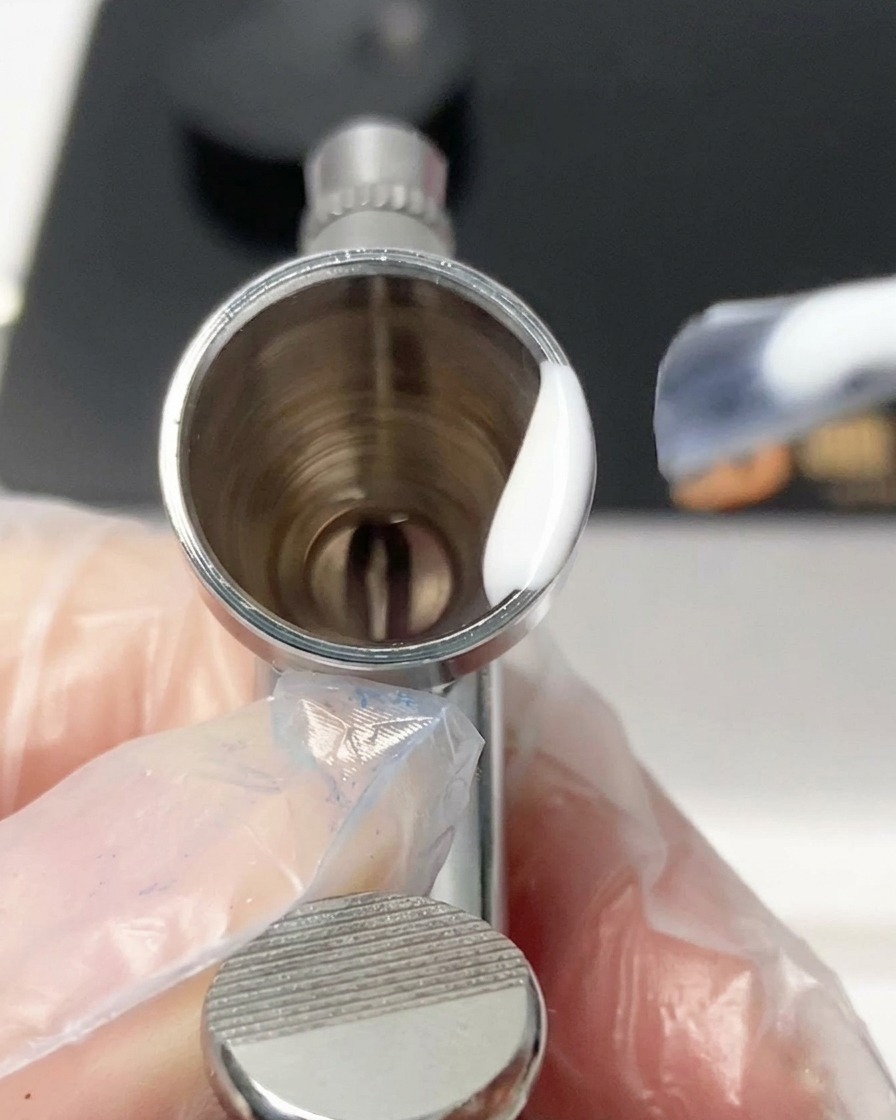A mixing tool blending white gel and thinner inside the airbrush reservoir.
