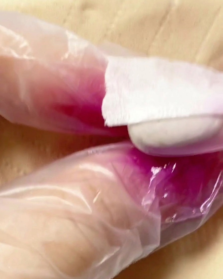 An airbrush tool applying a purple pigment mist onto the second half of a nail tip.