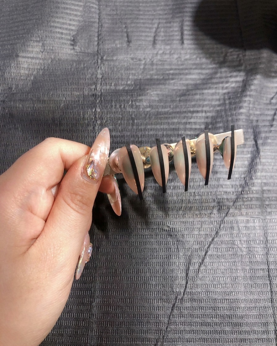 A close-up of a hand placing a thin black sticker vertically onto a nude-colored nail.