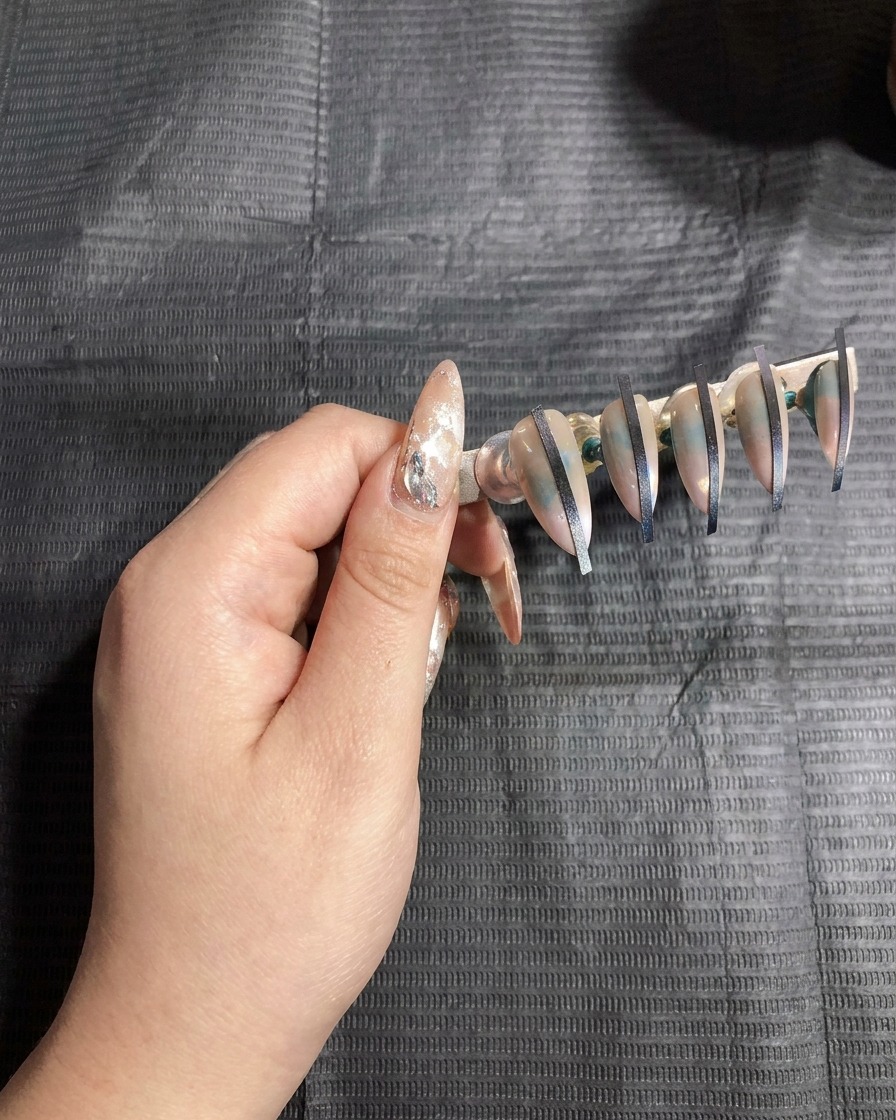 A nail stand with attached artificial nails placed inside a UV lamp for curing.