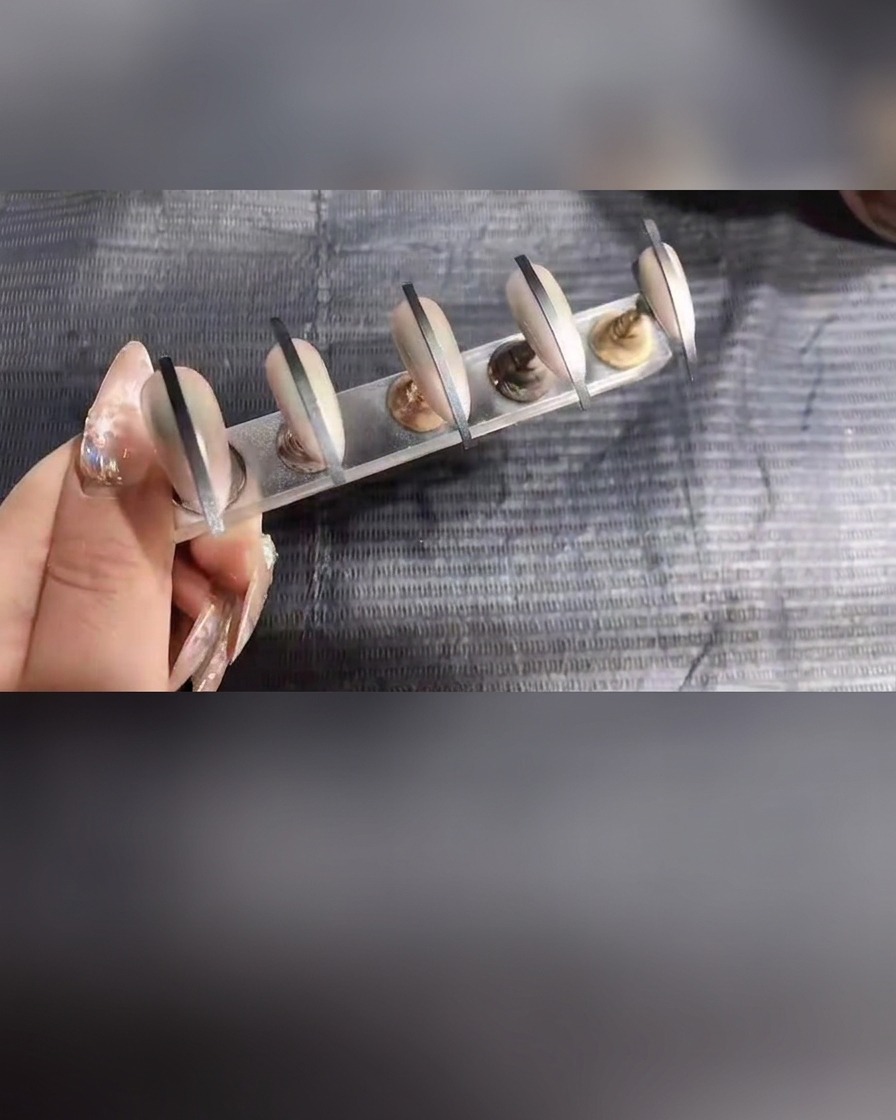 Close-up of nails on a stand receiving a final light application of spray gel.