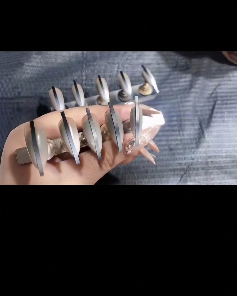 A pair of tweezers carefully removing a thin adhesive sticker from a finished airbrushed nail.