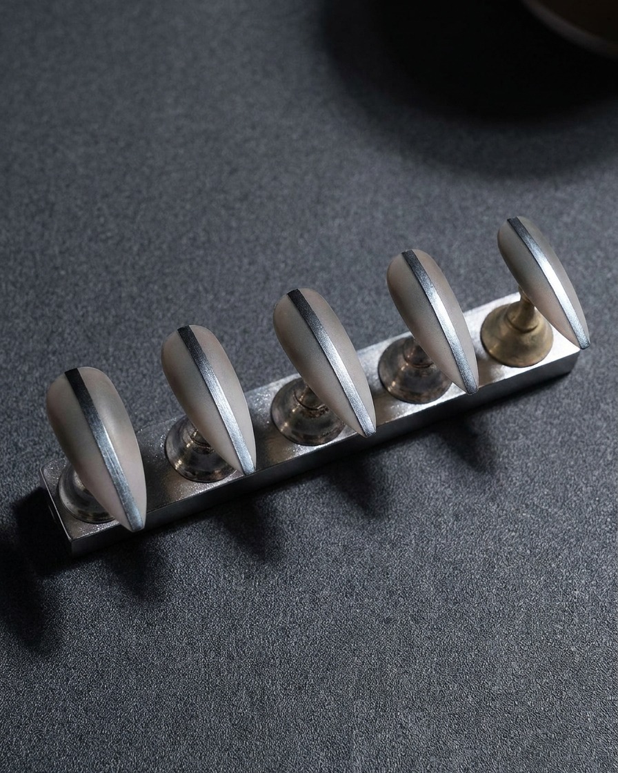 A close-up view of a metal nail stand holding five false nails, focusing on the refinement of the side edges using a file.