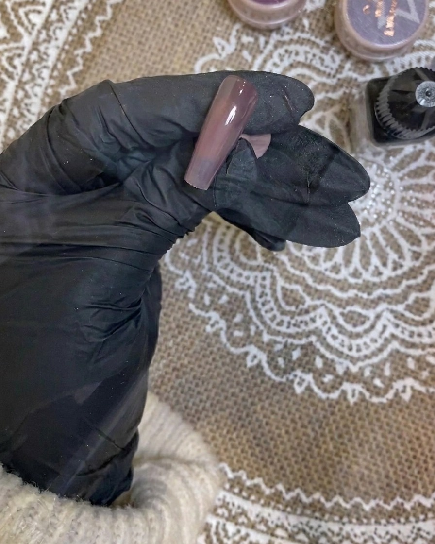 An airbrush being used to apply a soft white gradient to the tip of a dark purple nail.