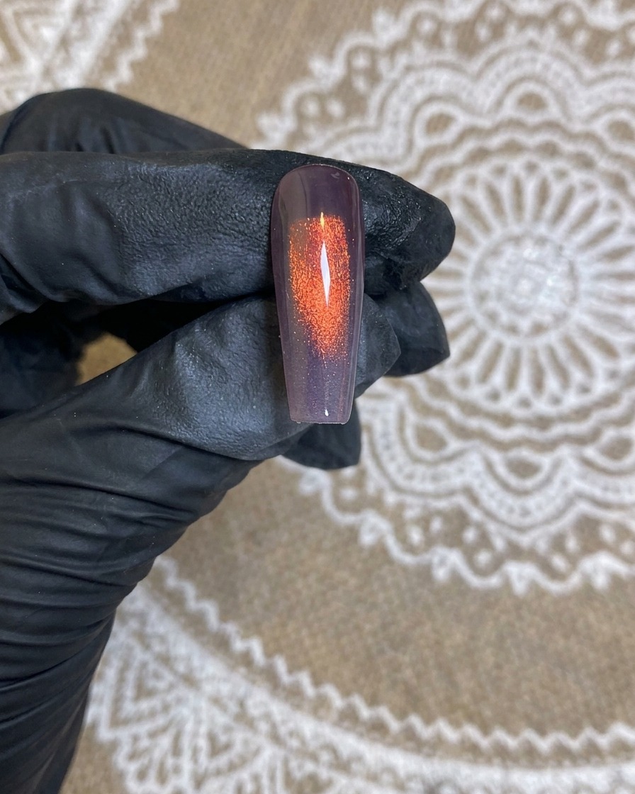 A close-up view of an airbrush nozzle spraying a white gradient onto a dark base nail.