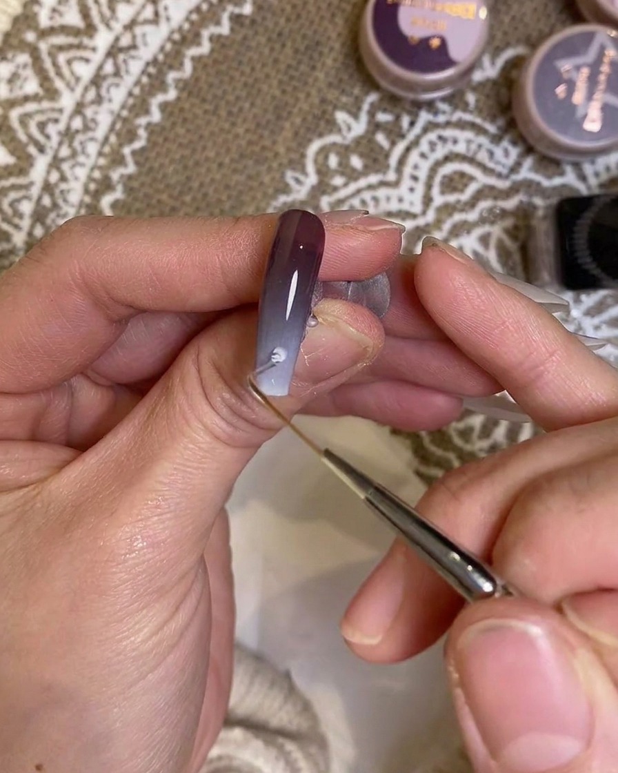 A detail brush carefully applying color near the cuticle area of the nail.