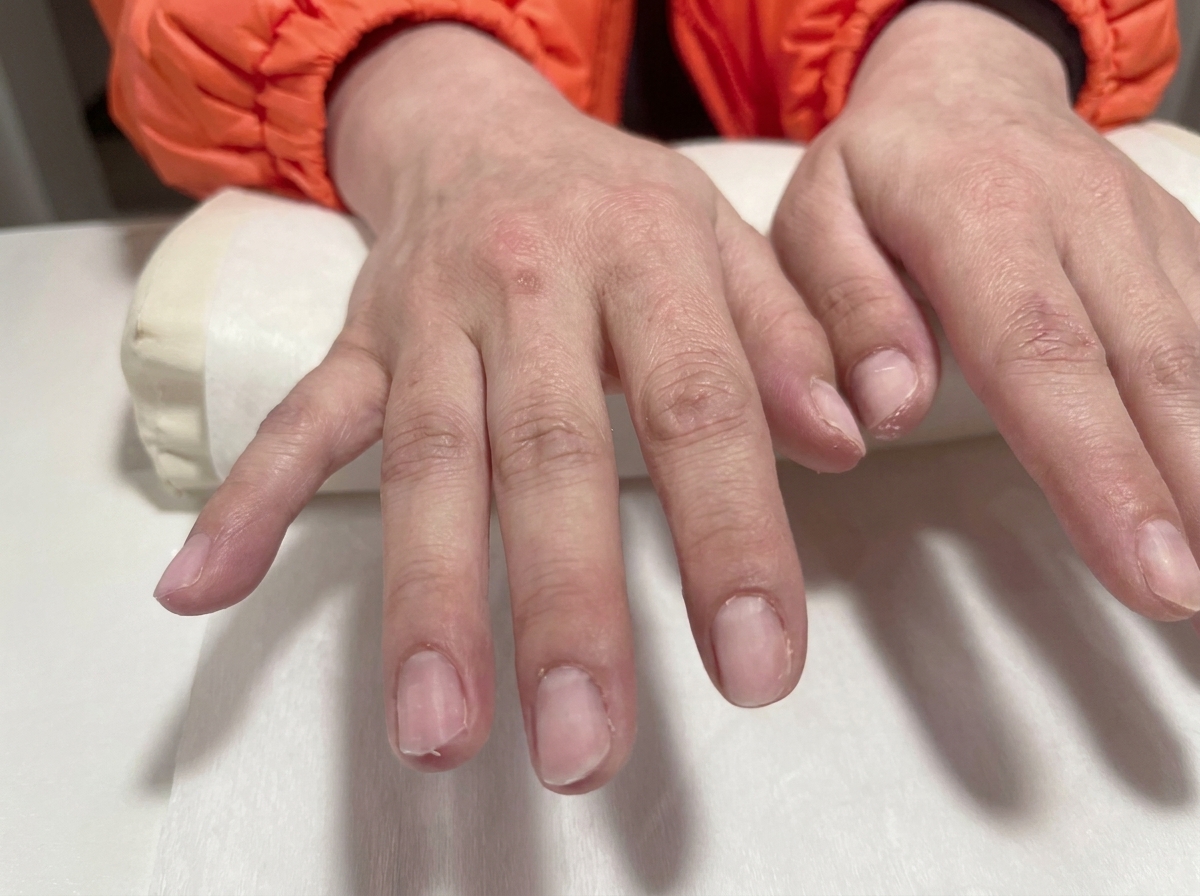 A close-up view of two hands with prepped, clear gel nails resting on a white salon cushion.