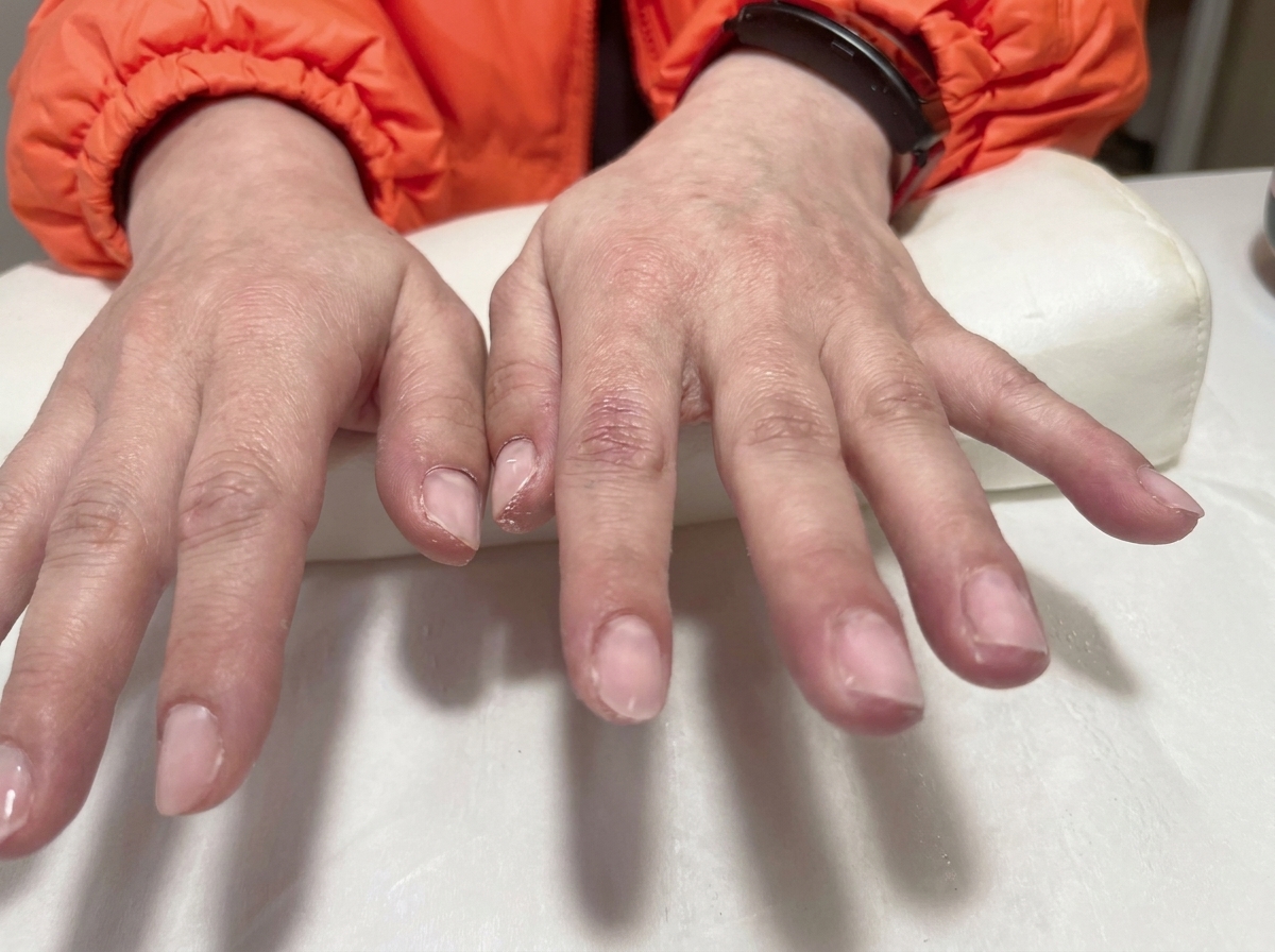 A close-up of a tool placing a tiny gold bow charm onto a nail surface.