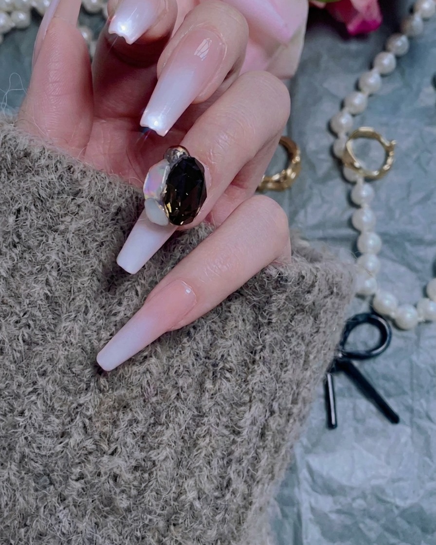 A hand using a nail file to gently buff the surface of a clear nail extension.