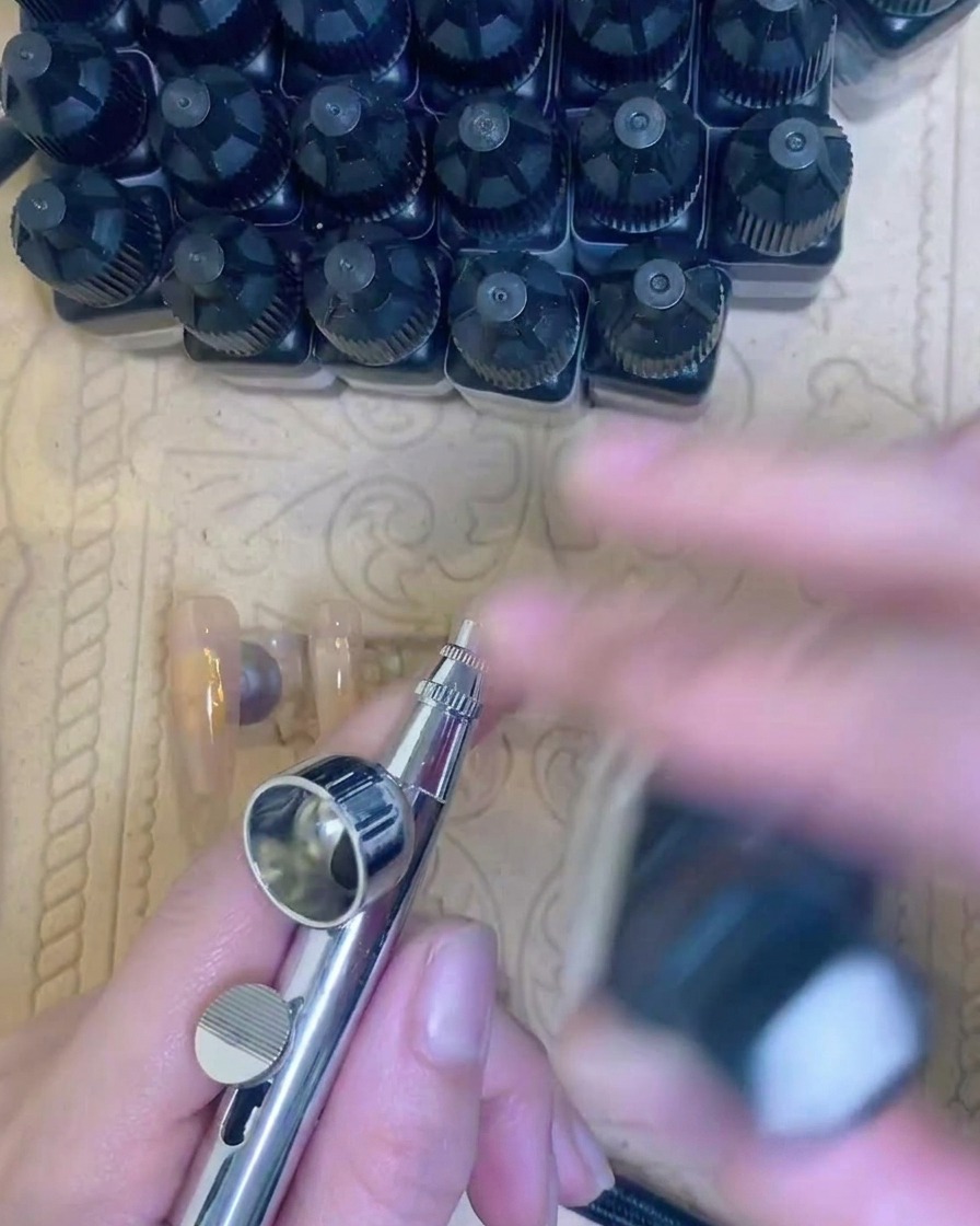 A close-up view of a brush applying a clear gel base coat to the natural nail.