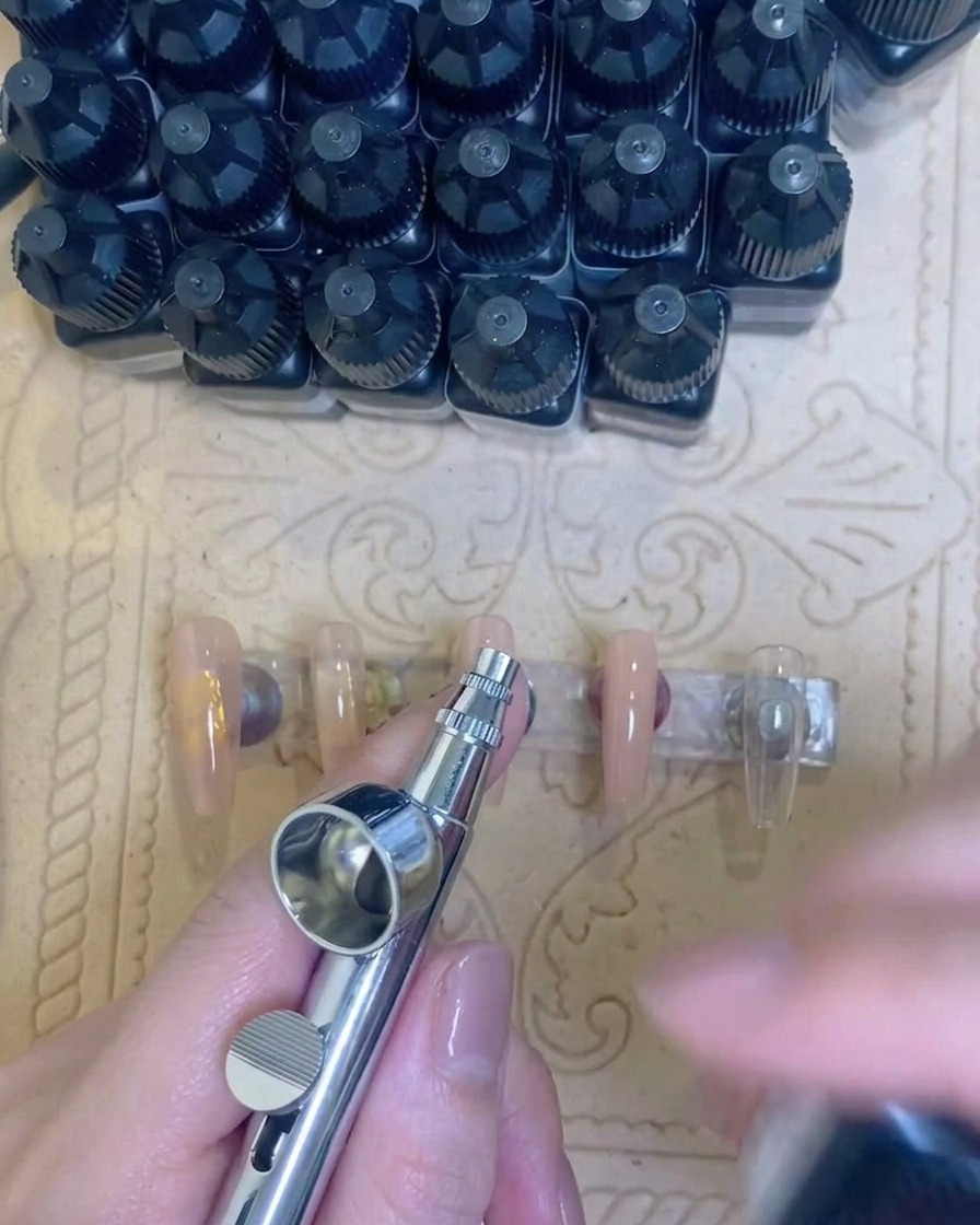 An airbrush tool spraying a test line of white pigment onto a piece of white paper towel.