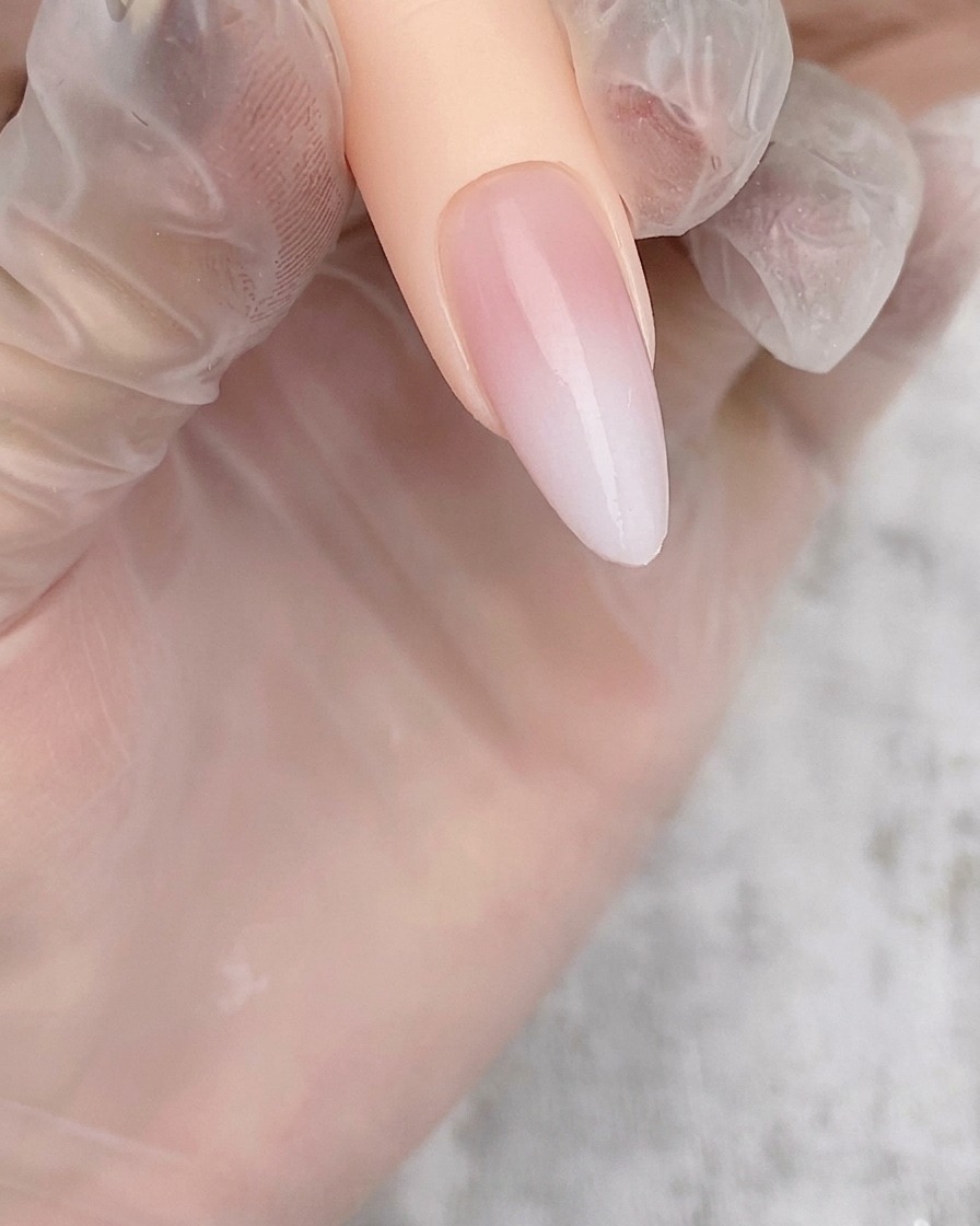An almond-shaped nail tip showing a soft, sheer white airbrush gradient applied over a nude base.