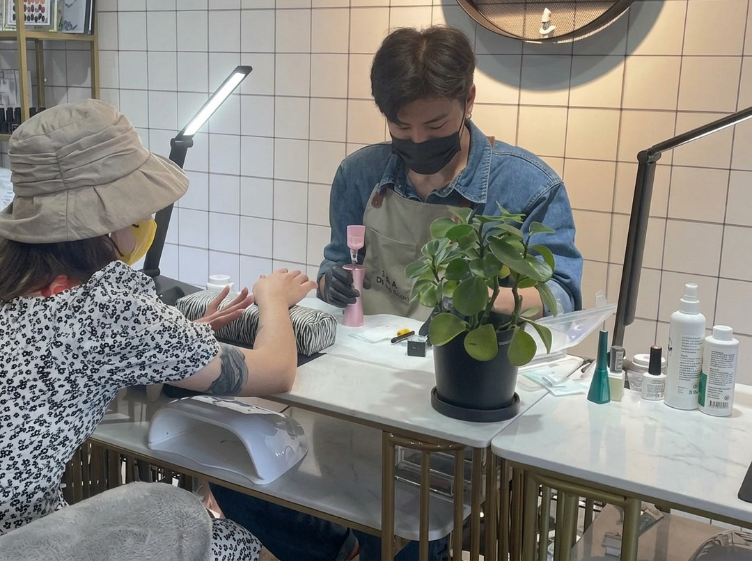 A close-up of a nail technician using a small brush to carefully apply clear base gel onto a clients fingernail.