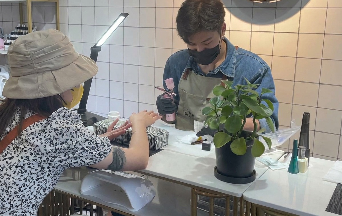A nail technician holding an airbrush tool and testing the spray on a piece of white tissue.